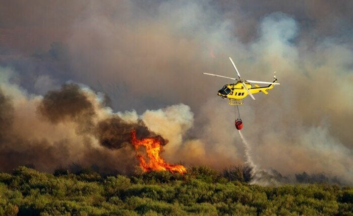 yellow helicopter releasing water on wildfire