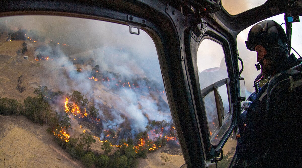 man looking down at wildfire from helicopter